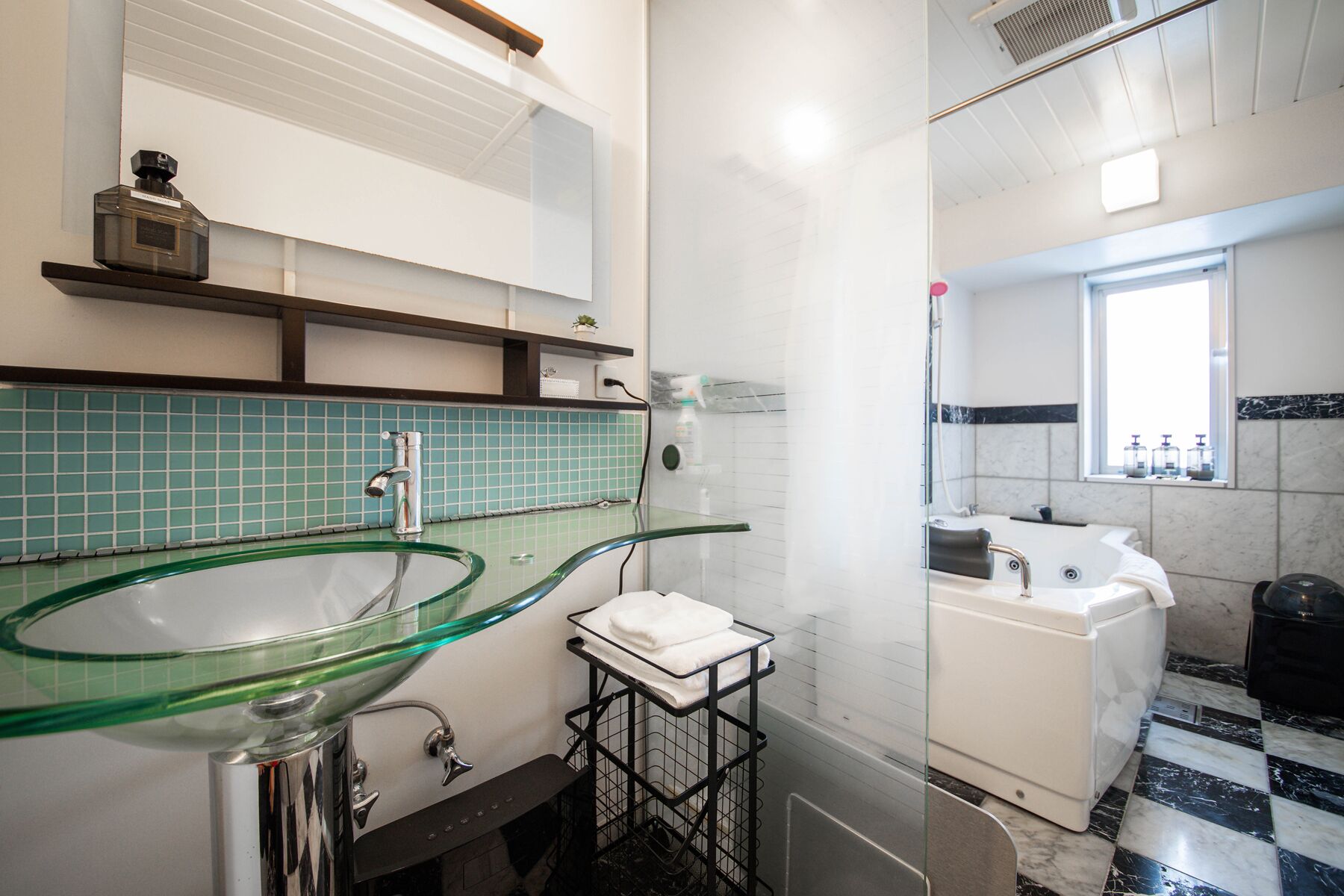 A modern bathroom with a glass sink, a white bathtub, and a shower area.