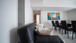 En moderne stue med en sort lædersofa, et spiseområde med sorte stole og et stort abstrakt billede på væggen.