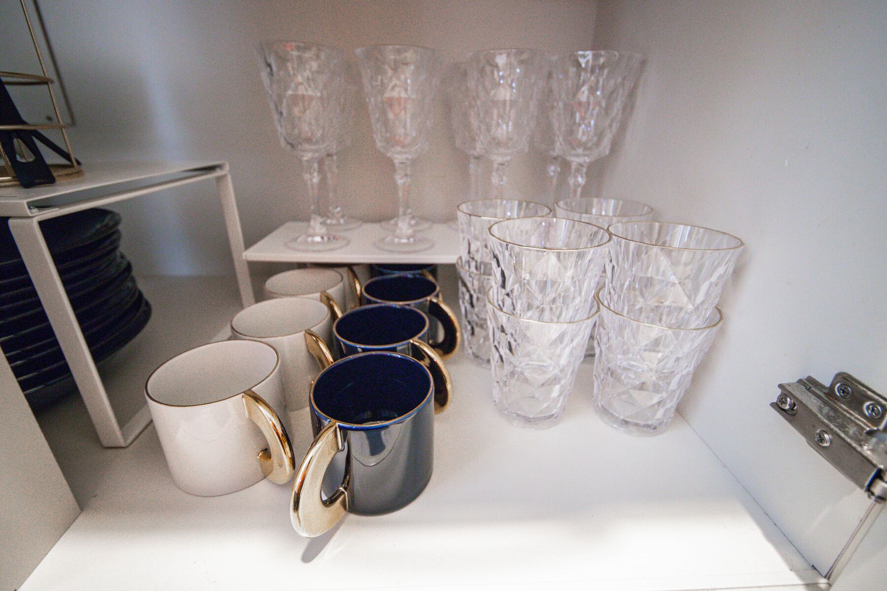 Et opbevaringsområde med forskelligt glas, herunder vinglas og drikkeglas, pænt arrangeret på hylder og et bord.