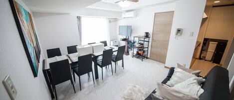 A modern living room with a black sofa, a dining area with a white table and chairs, and a ceiling fan.