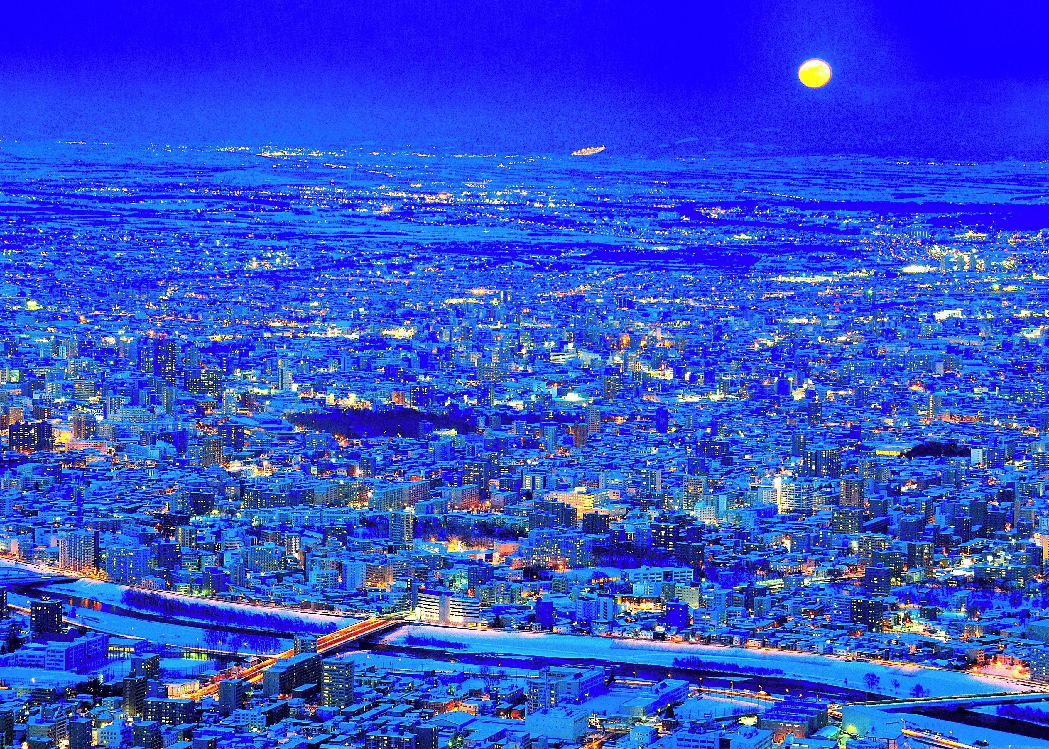 A cityscape at night with a prominent moon in the sky.