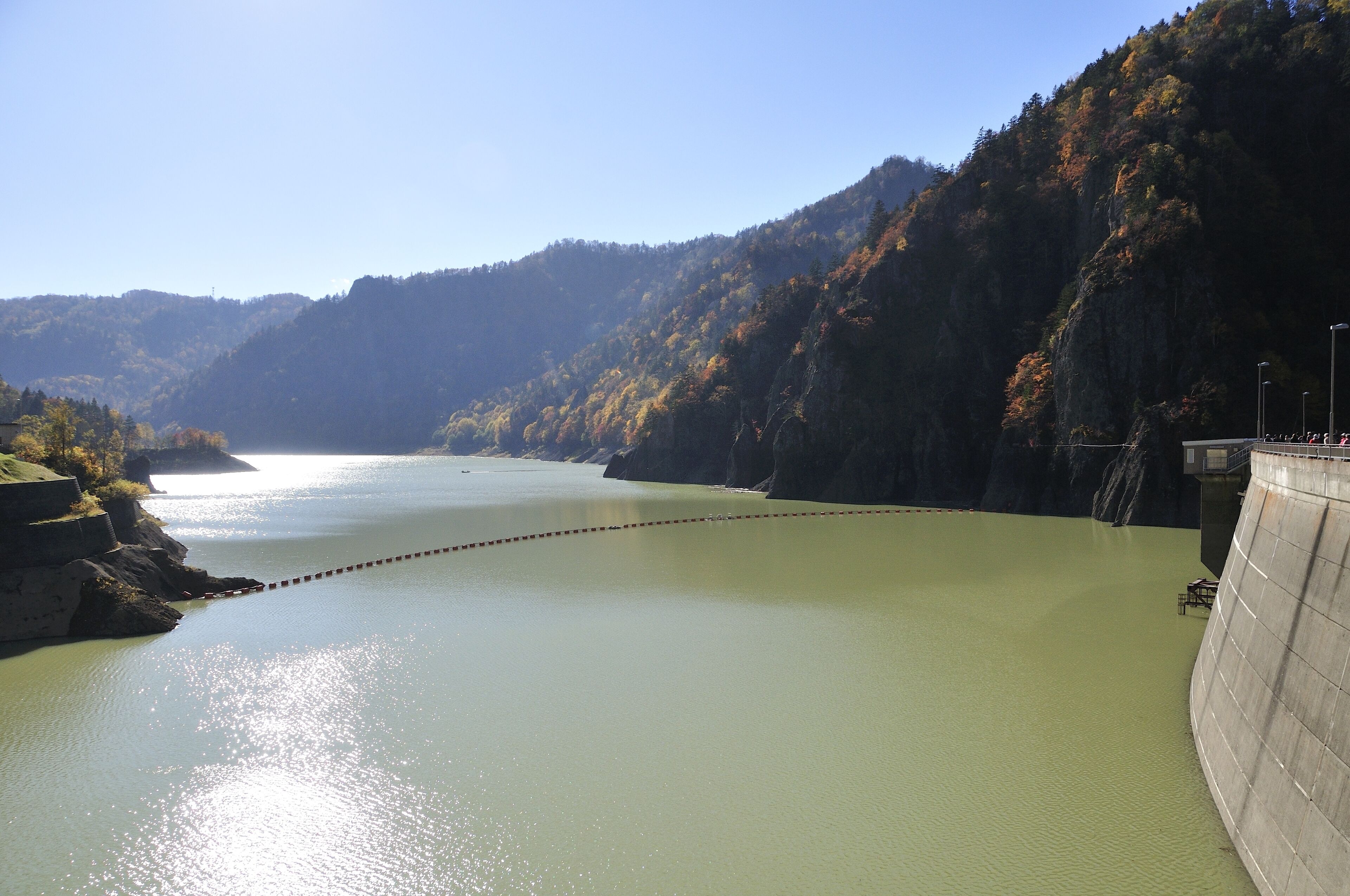 A dam with a lock system, a calm river, and surrounding forested hills.
