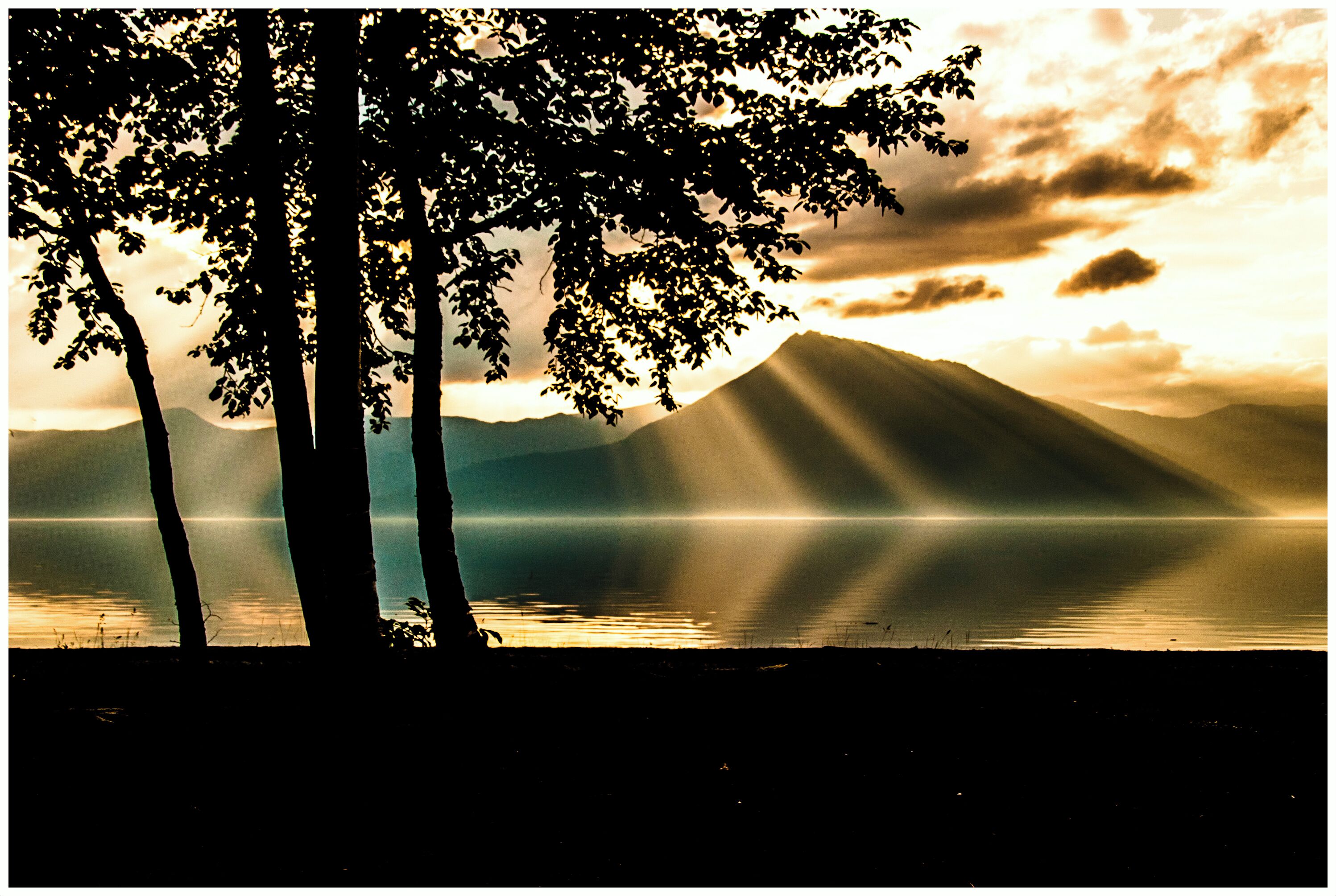 Une vue paisible sur un lac, avec les silhouettes des montagnes et les rayons du soleil.