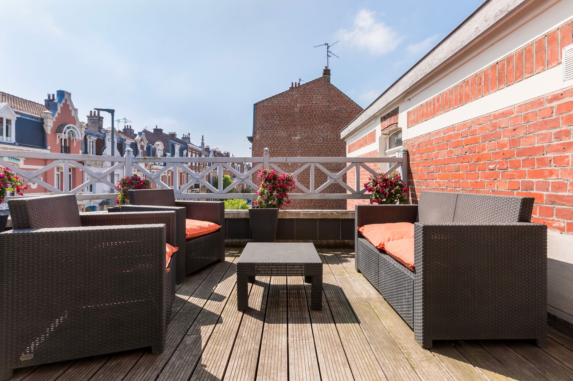 Eine Dachterrasse mit Korbmöbeln, einem Holztisch und Topfpflanzen.