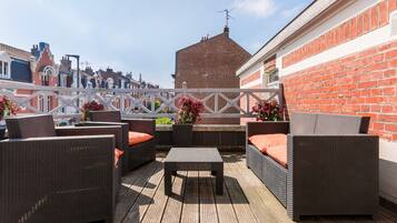 Eine Dachterrasse mit Korbmöbeln, einem Holztisch und Topfpflanzen.