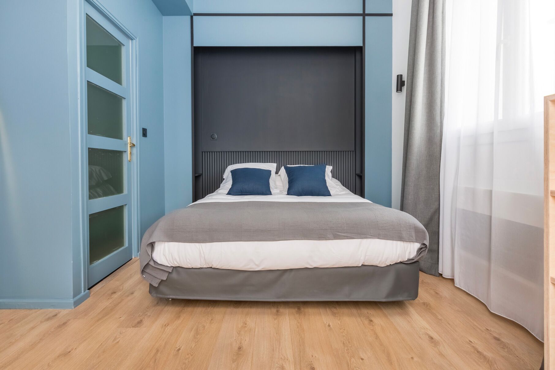 A modern bedroom with a bed, a wardrobe, and a door.