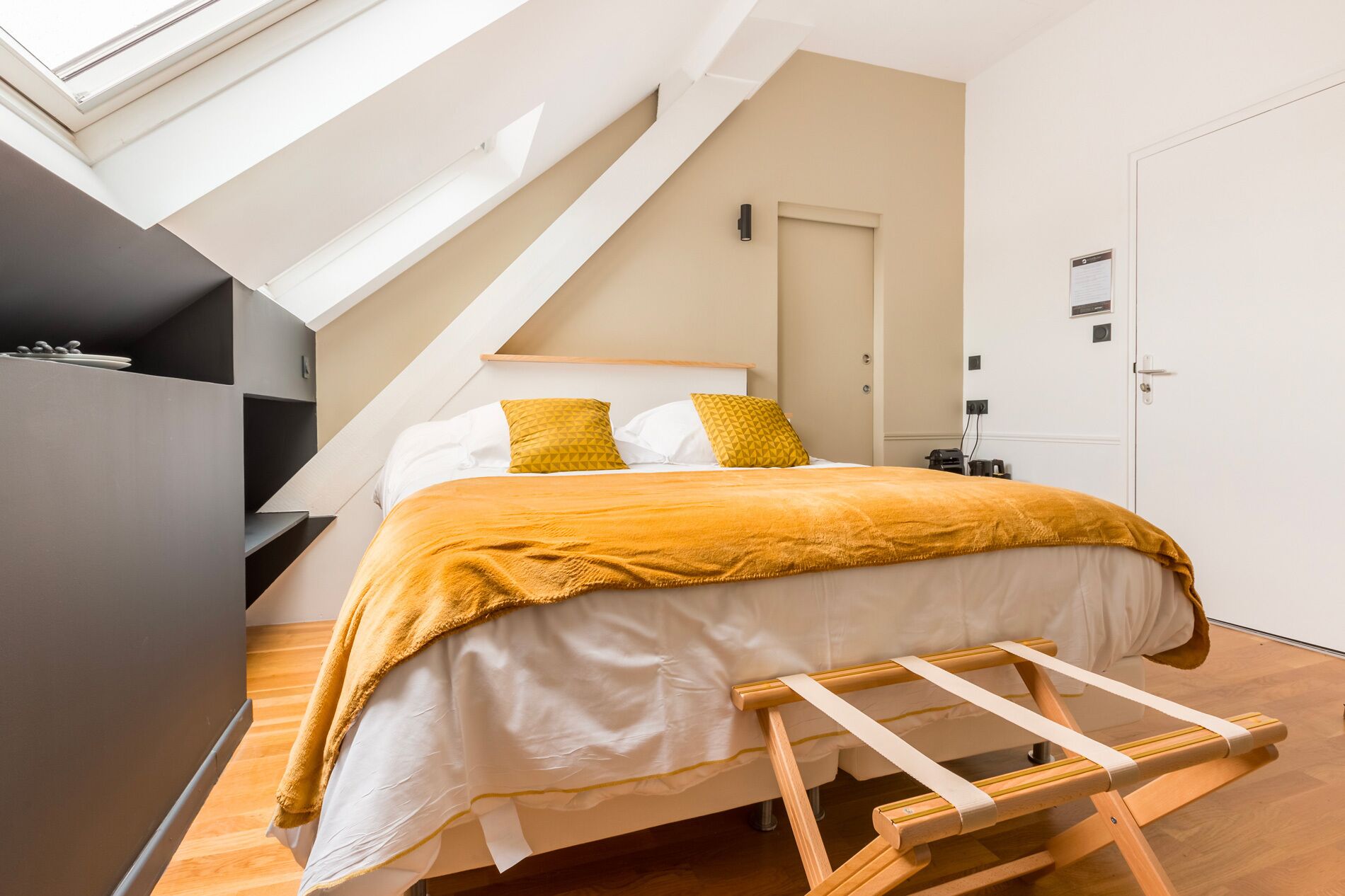 Une chambre moderne avec un plafond en pente, un lit recouvert d’une couverture de couleur moutarde et une échelle en bois.