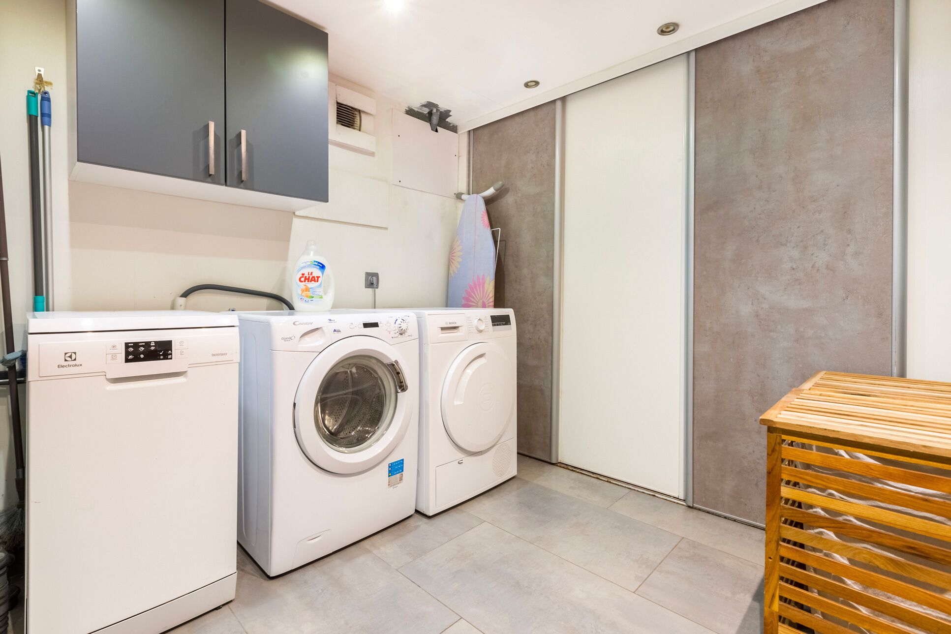 A laundry room with two washing machines, a drying rack, and a bottle of detergent.