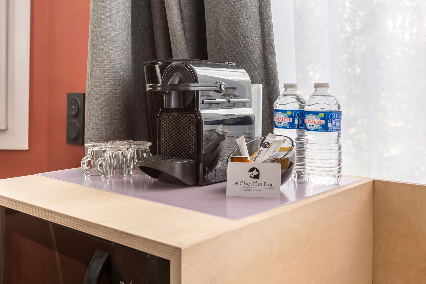 Ein Schreibtisch im Hotelzimmer mit Kaffeemaschine, Gläsern, einer Reihe von Pflegeprodukten und Wasserflaschen.