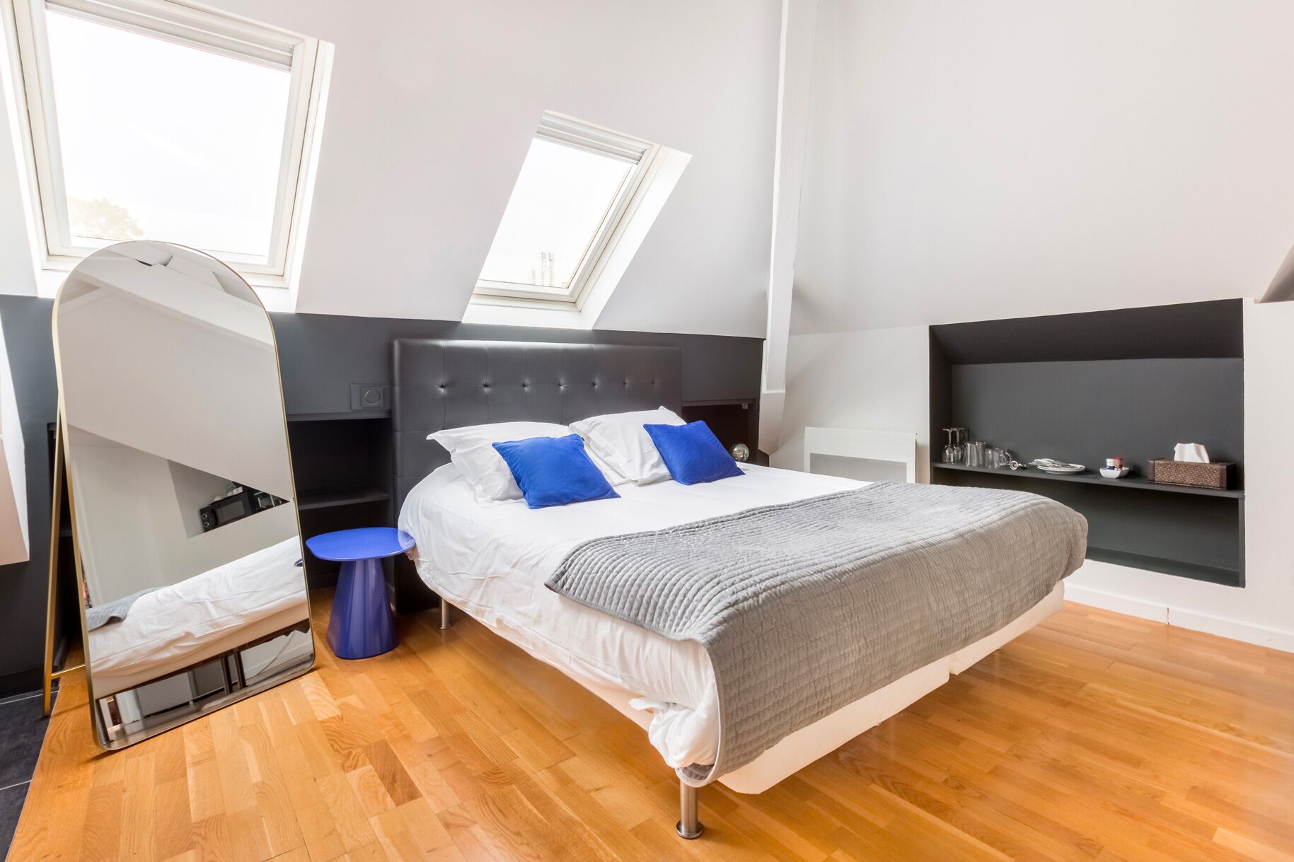 Een moderne slaapkamer met een groot bed, dakraam, een klein rond tafeltje en een ingebouwde plank met keukengerei.
