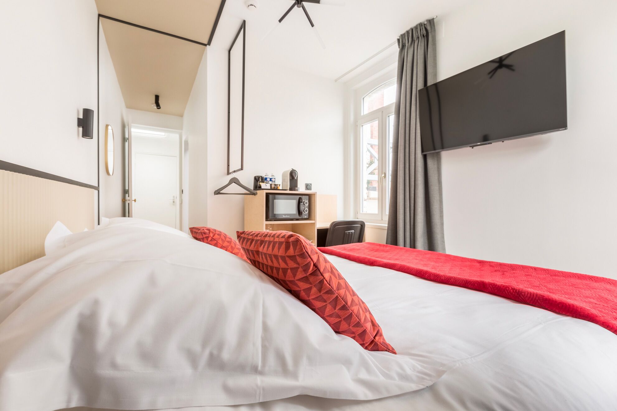 Ett hotellrum med en säng, en tv som är monterad på väggen, en mikrovågsugn och ett litet skrivbord med en stol.