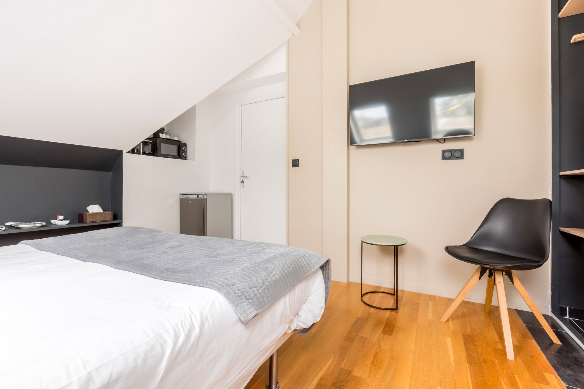 A modern bedroom with a bed, a TV, a small fridge, a microwave, and a chair.