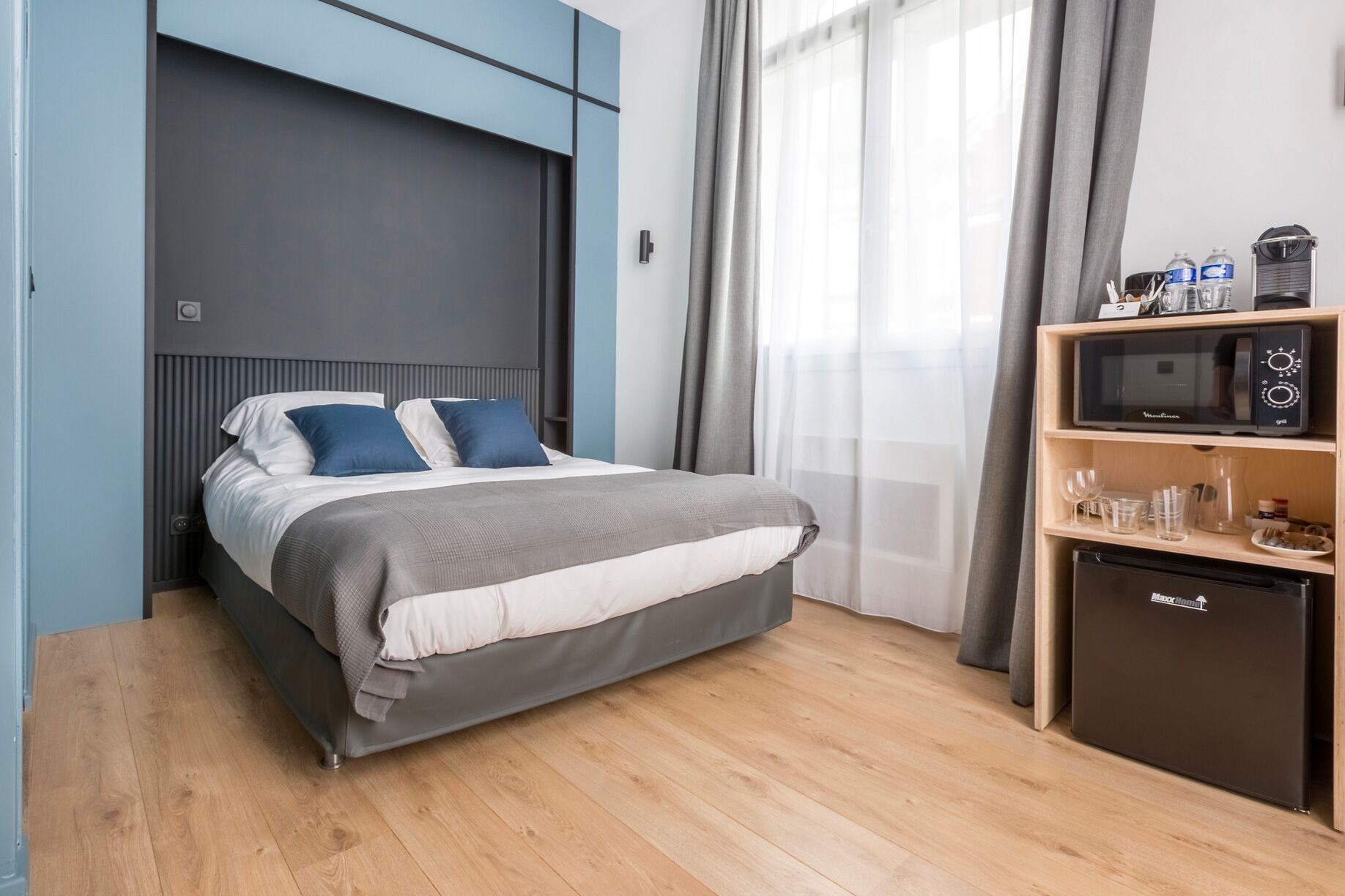Ein modernes Schlafzimmer mit Bett, integriertem Fernseher, Minibar und einem Vorhangfenster.