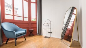 A room with a blue armchair, a tall mirror, and a wooden floor.