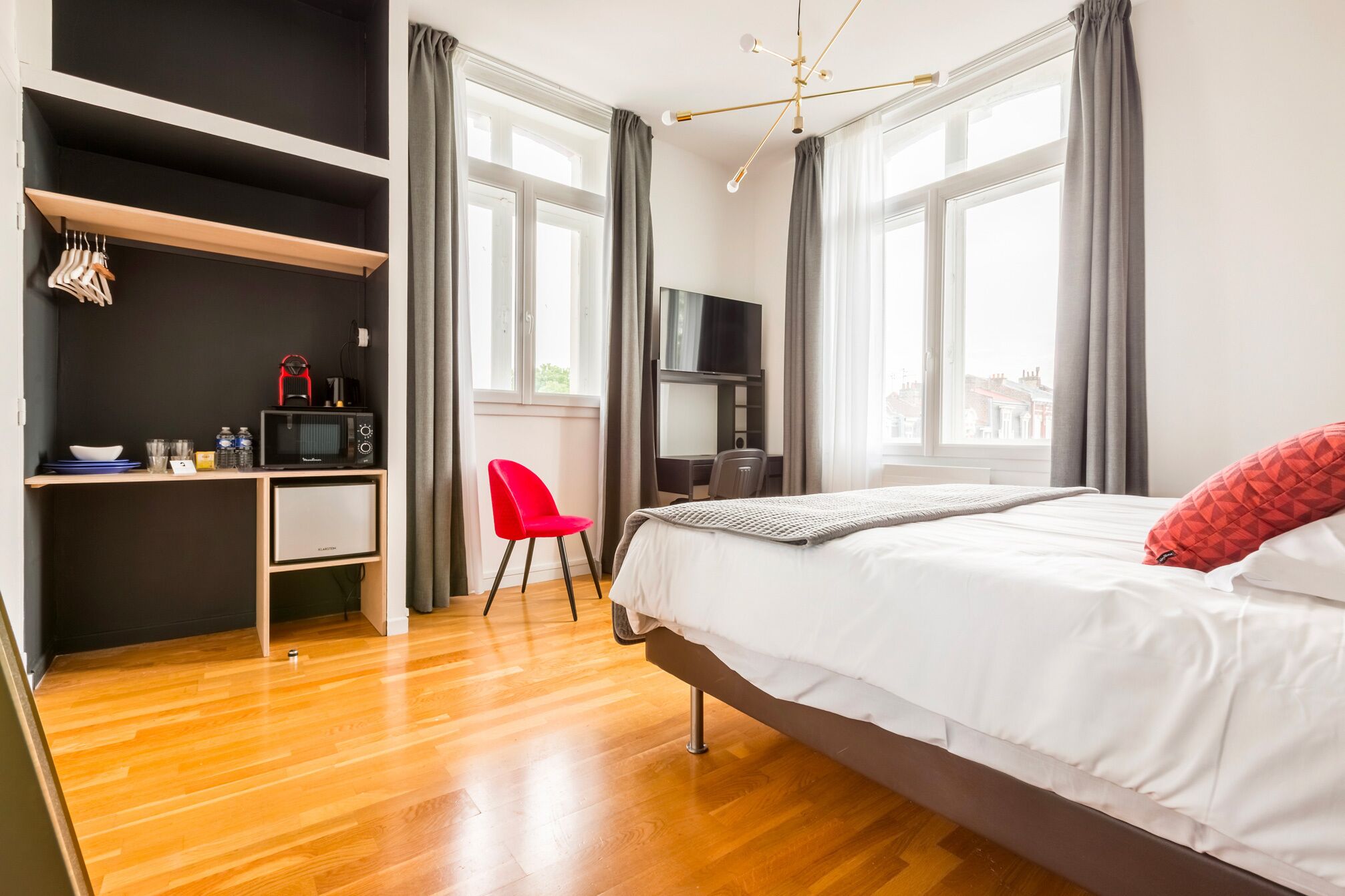 A hotel room with a bed, a desk with a chair, a TV, and a minibar.