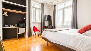 A hotel room with a bed, a desk with a chair, a TV, and a minibar.