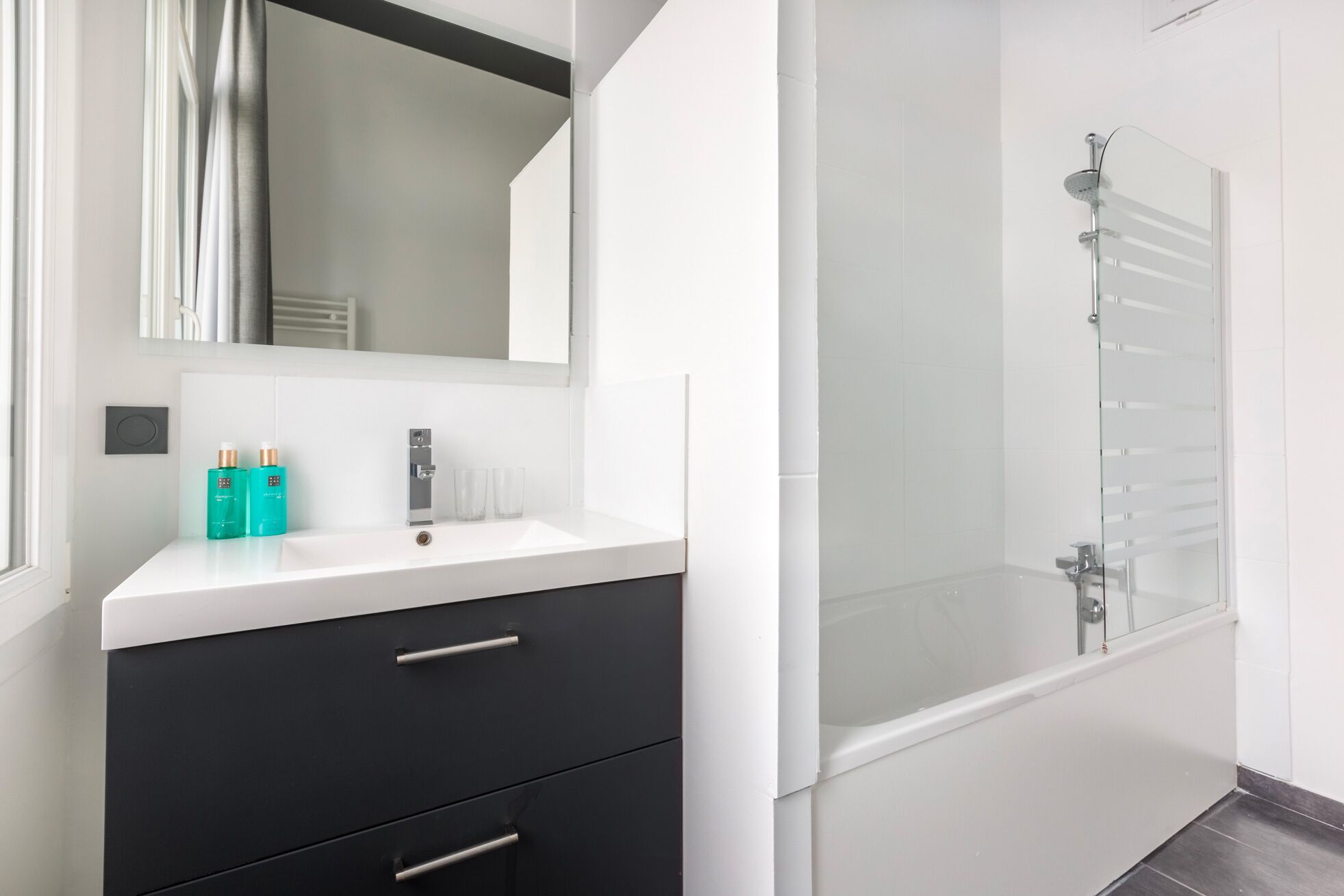 A modern bathroom with a white vanity, black drawers, a large mirror, and a glass-enclosed shower area.