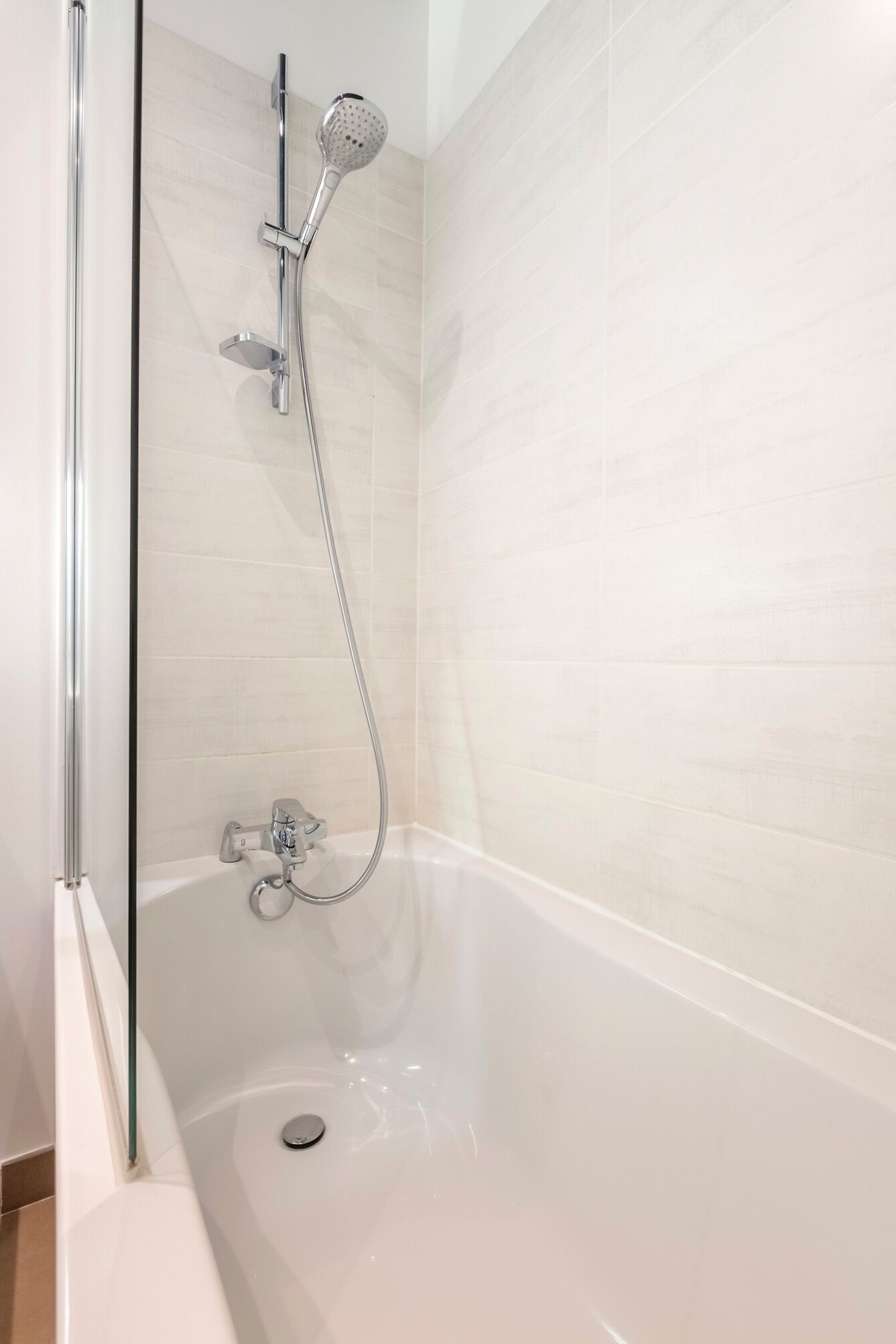 Een moderne badkamer met een douchecabine van glas, een witte badkuip en een verchroomde douchekop.