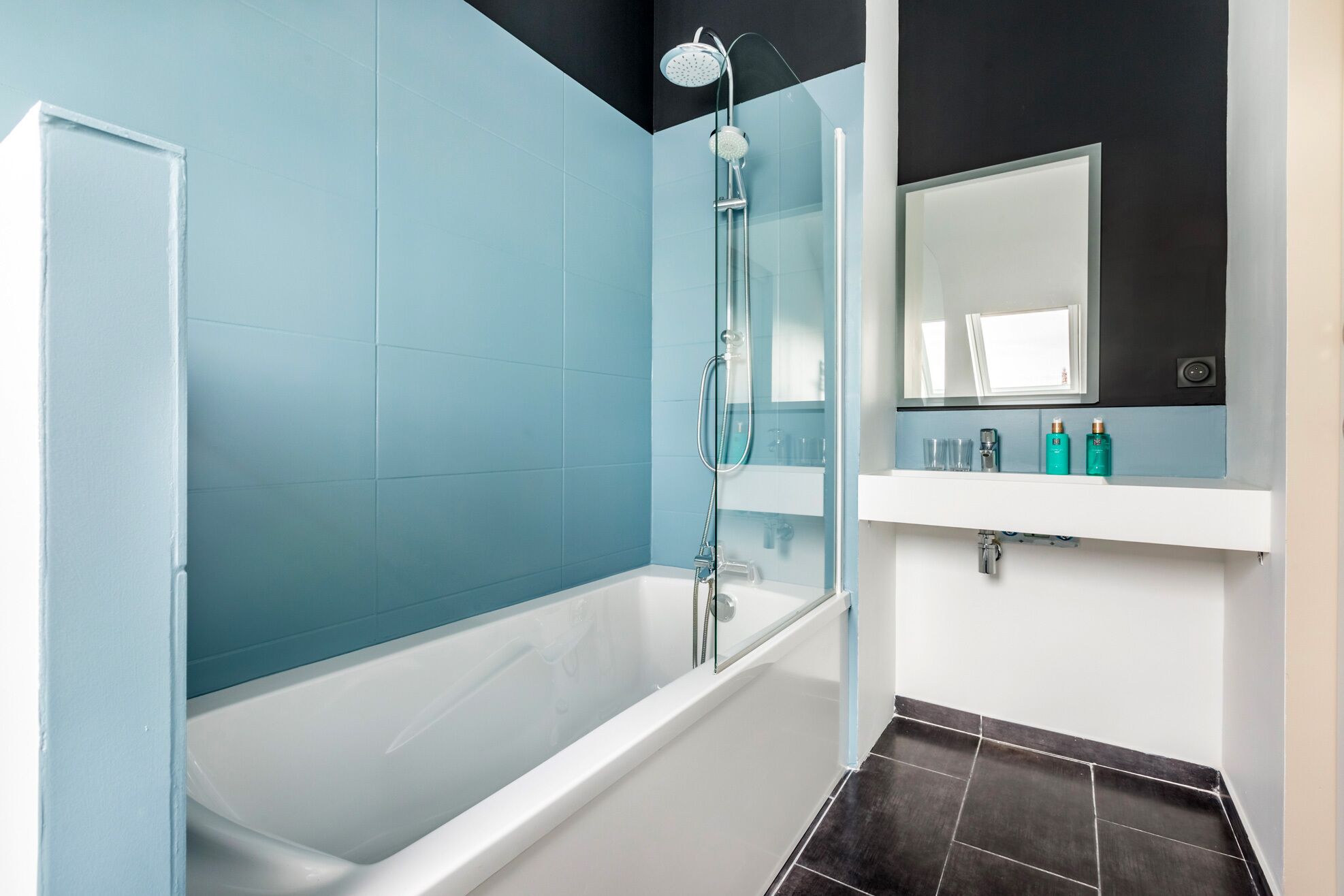 Un baño moderno con bañera, cabina de ducha de vidrio y tocador con espejo y artículos de aseo.