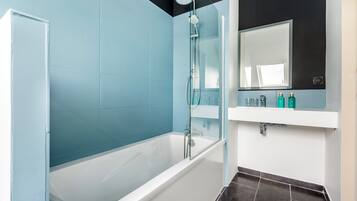 Un baño moderno con bañera, cabina de ducha de vidrio y tocador con espejo y artículos de aseo.