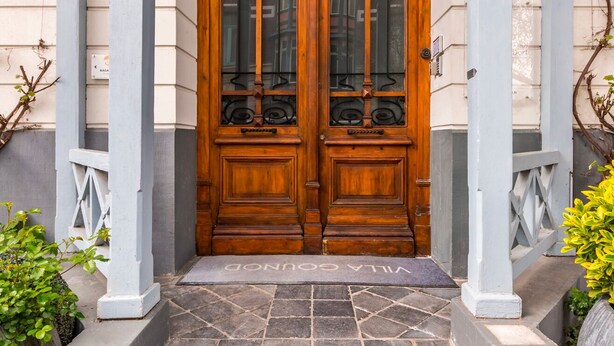 A wooden double door with glass panels, flanked by white columns, leading to a stone staircase.
