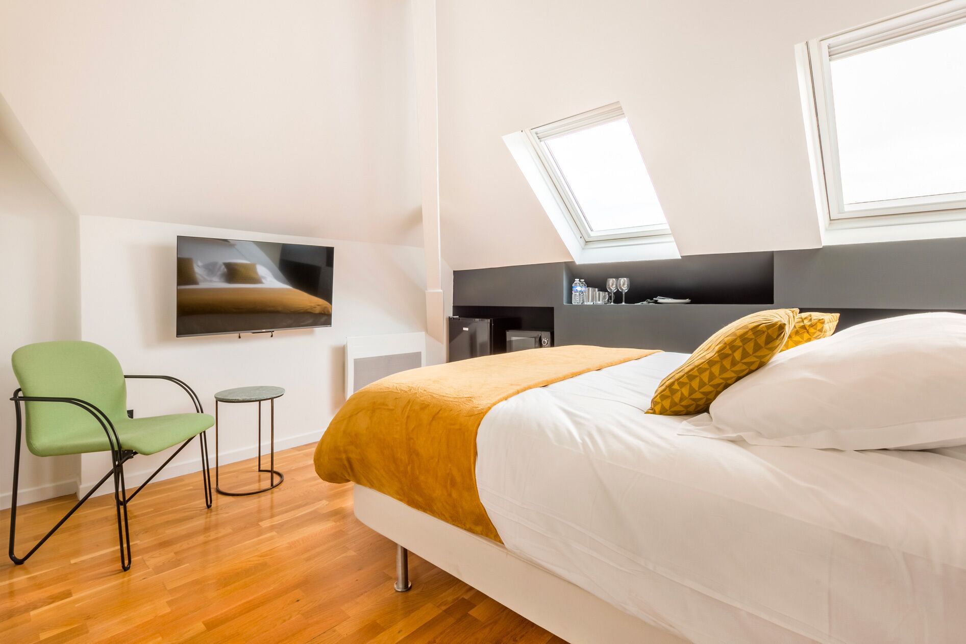 Een moderne hotelkamer met een bed, een groene stoel, een kleine tafel, een televisie en een dakraam.
