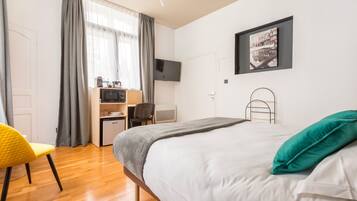 A modern hotel room with a bed, a desk with a microwave, a chair, and a TV on the wall.