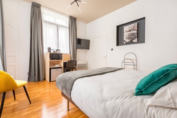 A modern hotel room with a bed, a desk with a microwave, a chair, and a TV on the wall. - Au Chat Qui Dort Lille - Villa Gounod (Lille)