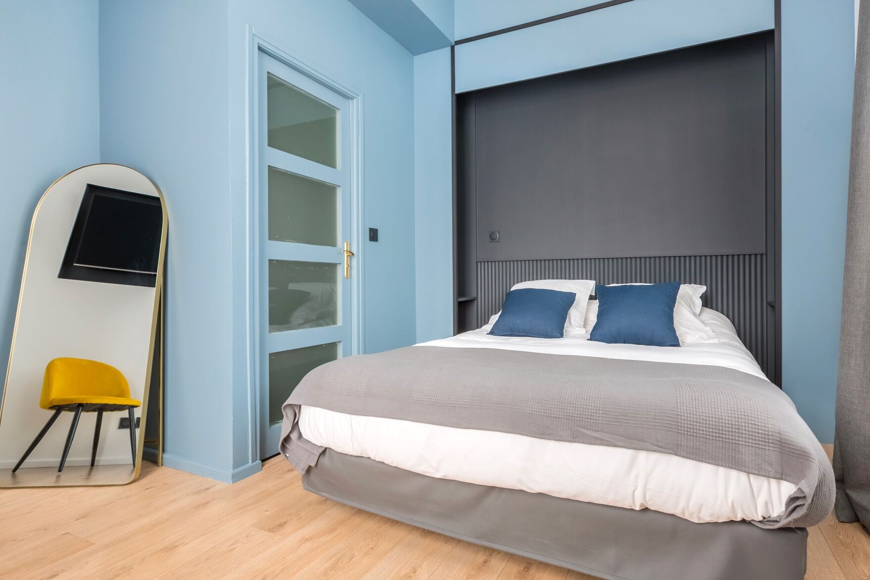 Un dormitorio moderno con cama, televisión montada en la pared y una silla amarilla.