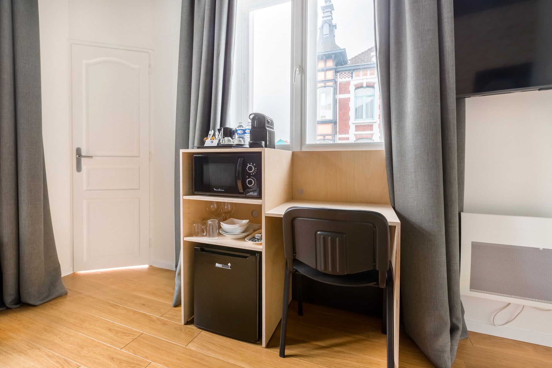 Una habitación compacta con kitchenette, microondas, refrigerador pequeño, escritorio y una silla.