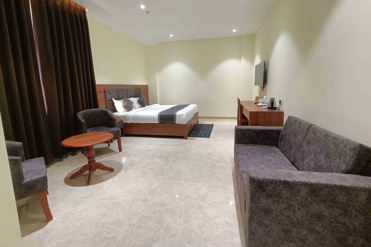A hotel room with a bed, a sofa, a chair, a small table, a TV, and a curtain.