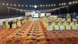 Une salle de banquet avec des rangées de chaises recouvertes de nappes jaunes et rouges, une moquette à motifs et des guirlandes lumineuses suspendues au plafond.