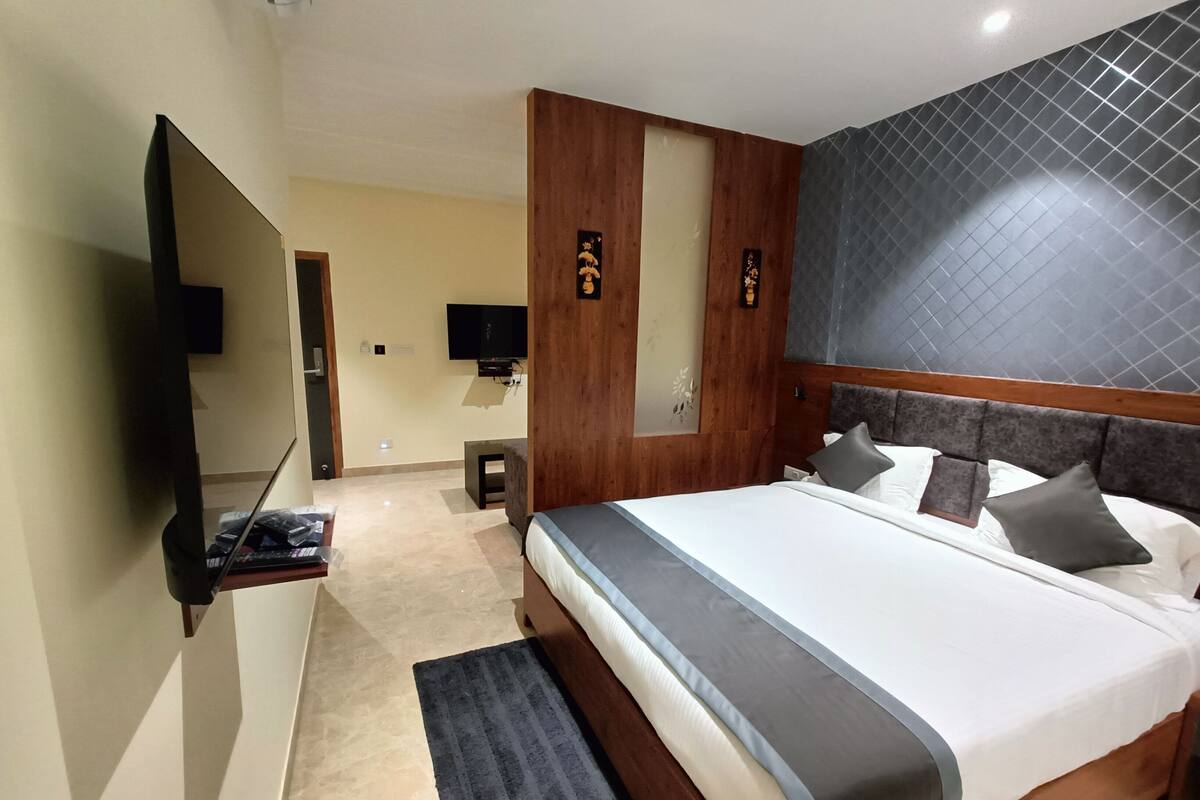 A modern hotel room with a large bed, a flat-screen TV, a wooden accent wall, and a small seating area.