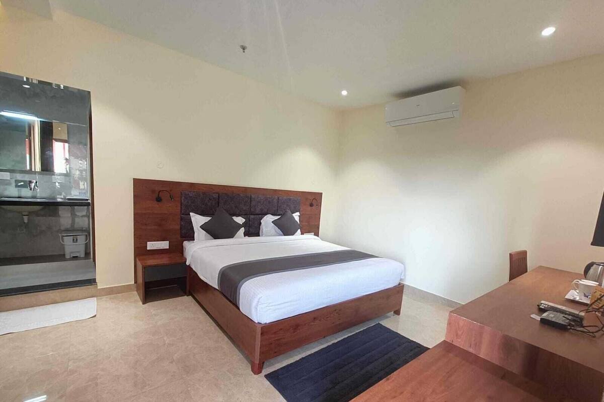 A modern hotel room with a wooden bed, a small desk, and a bathroom with a mirror and sink.