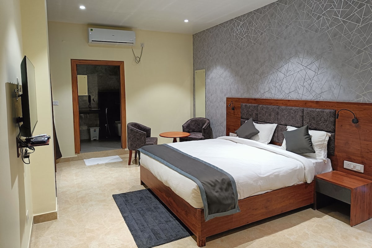 A modern hotel room with a large bed, bedside tables, a small round table, and a seating area with chairs.