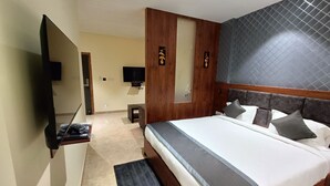 Une chambre d’hôtel moderne avec un grand lit, un téléviseur à écran plat fixé au mur, une tête de lit en bois et une petite table de chevet.