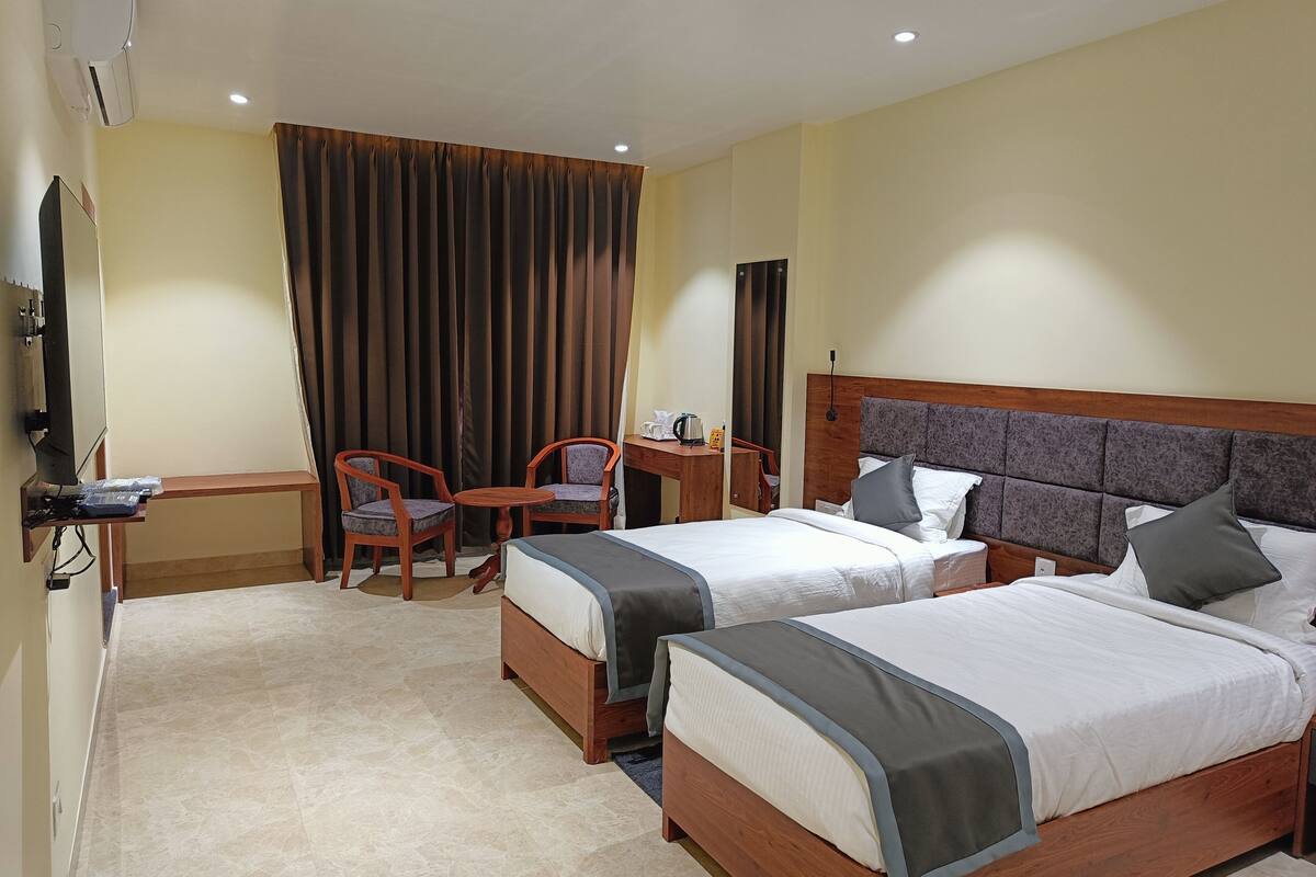 A hotel room with two beds, a desk, a chair, a TV, and a curtain.
