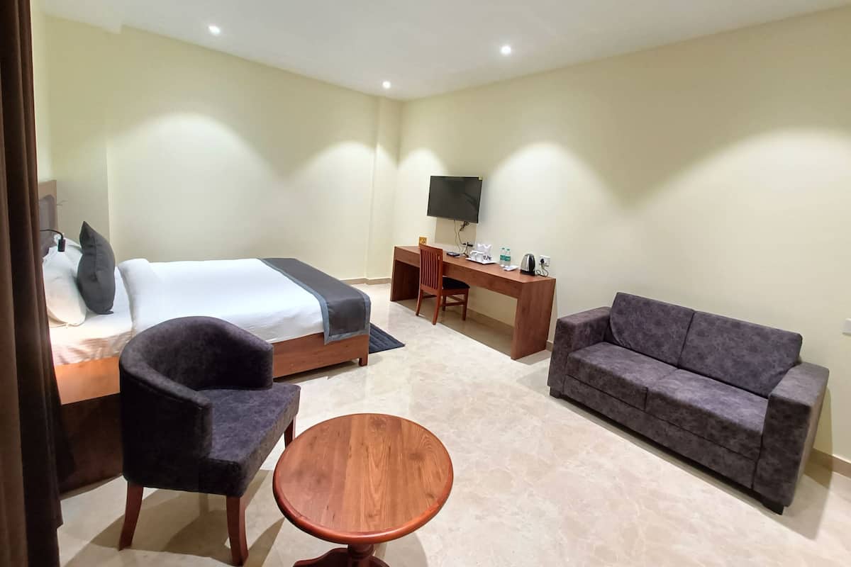A hotel room with a bed, a desk, a television, a sofa, and a small round table.