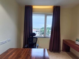 Habitación de hotel con un escritorio de madera, una silla, un banco y una ventana con cortinas.