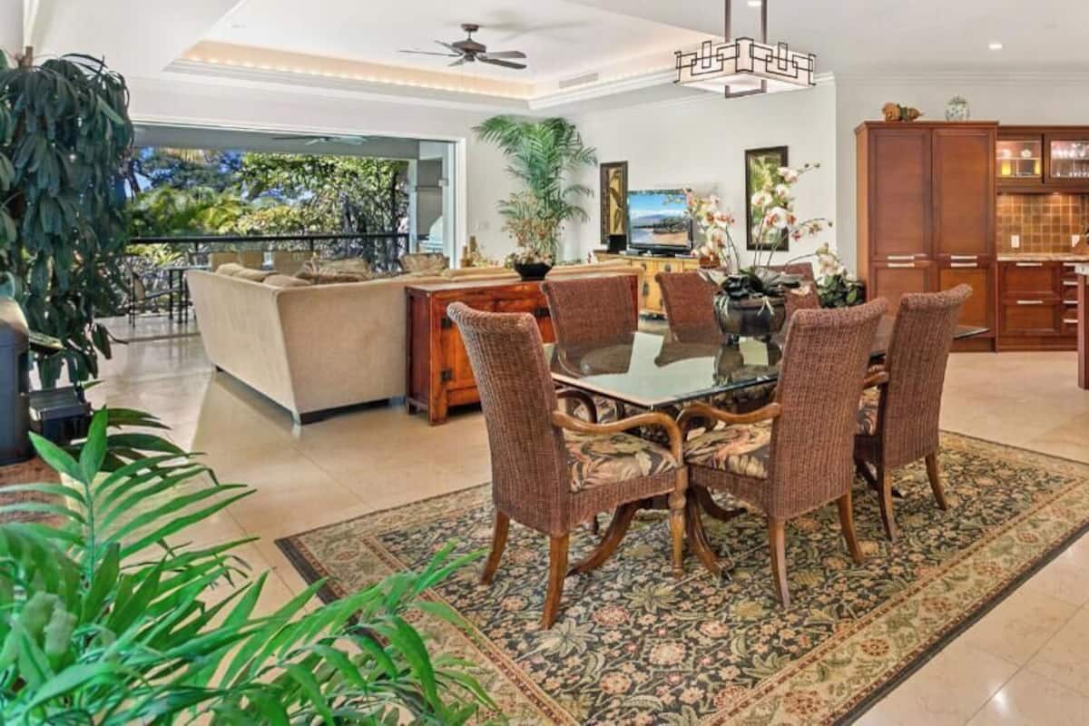 Amplia sala de estar con una mesa de comedor rodeada de sillas, una cocina con armarios de madera y un balcón con plantas.