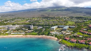 A coastal resort with multiple buildings, a beach, and a mountainous backdrop. - Ho'olei Garden View by Coldwell Banker Island Vacation (Kihei)