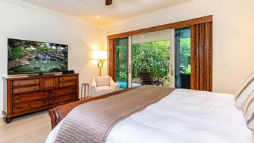 A bedroom with a bed, a TV on a wooden dresser, a chair, and a view of greenery through a glass door.
