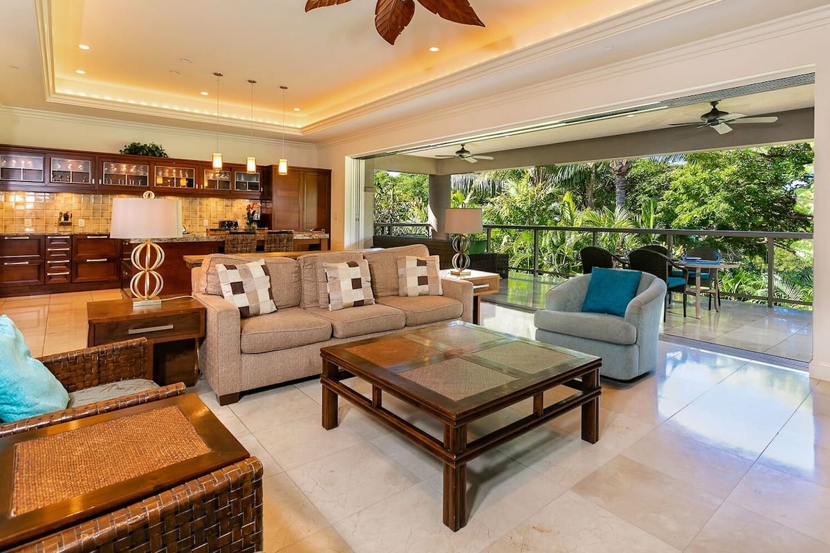 Amplia sala de estar con un conjunto de sofás, una mesa de centro y una mesa de comedor. Cuenta con una cocina con armarios y vistas al exterior.
