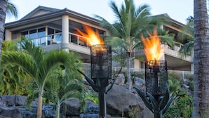 A hotel with a modern design, featuring two prominent torches with flames, a waterfall, and a balcony overlooking the landscape. - Ho'olei Garden View by Coldwell Banker Island Vacation (Kihei)