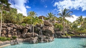 A resort pool with clear water, surrounded by rocks and palm trees, and a building in the background. - Ho'olei Garden View by Coldwell Banker Island Vacation (Kihei)