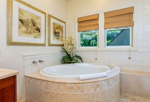 Une salle de bain dotée d’une grande baignoire, d’œuvres d’art encadrées au mur et d’une fenêtre donnant sur un paysage verdoyant.