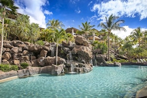 A resort pool with clear water, a rocky waterfall, and palm trees. - Ho'olei Garden View by Coldwell Banker Island Vacation (Kihei)