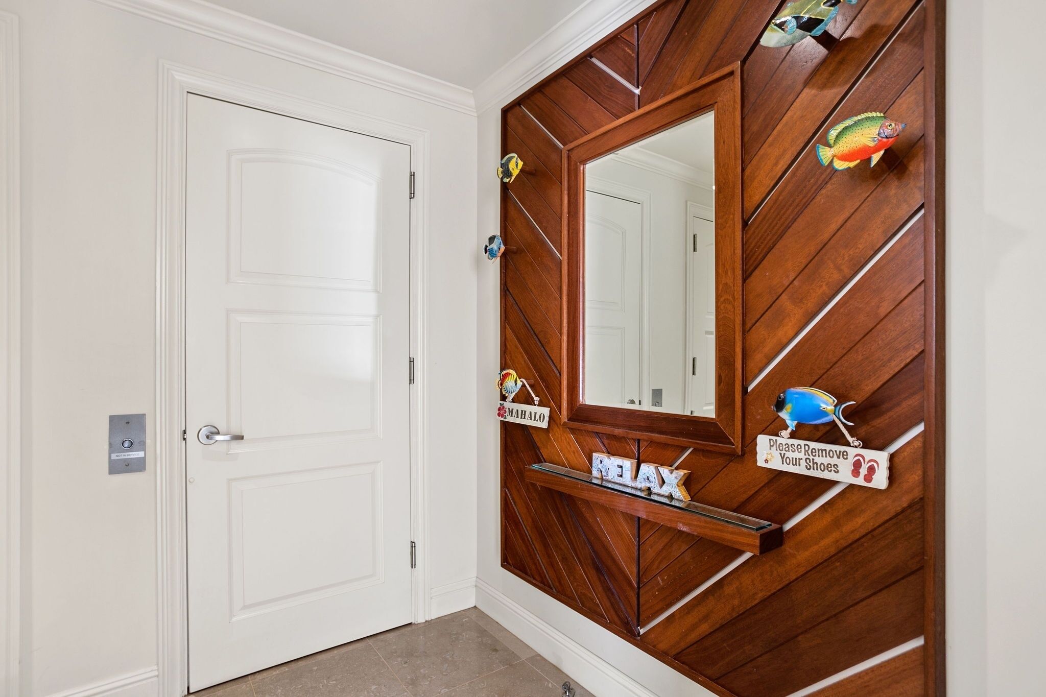 A hallway with a white door, a wooden wall with a mirror, and a sign requesting guests to remove their shoes.