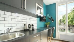 Een moderne keuken met een roestvrijstalen spoelbak, een waterkoker en een ingebouwde oven. Er staan twee barkrukken en er is een raam met uitzicht op buiten.