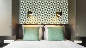 Een netjes opgemaakt bed met twee kussens, een behanget patroon op de muur en twee wandlampen.